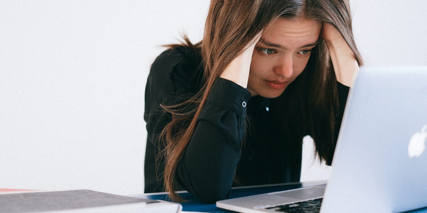 Nuori nainen istuu ahdistuneena tietokoneen ääressä pää käsiin painautuneena.