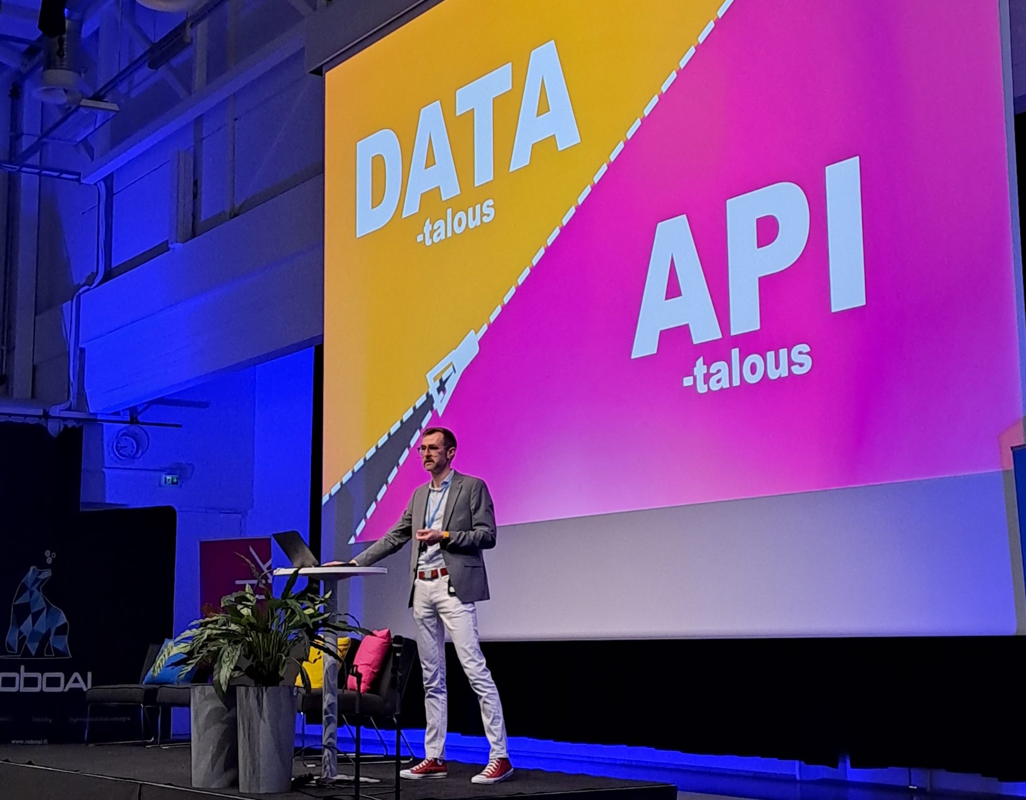 Research Manager Mikko Pakkasela stands on the stage to speak. In the background, the words Data economy and API economy are superimposed on a PowerPoint presentation.