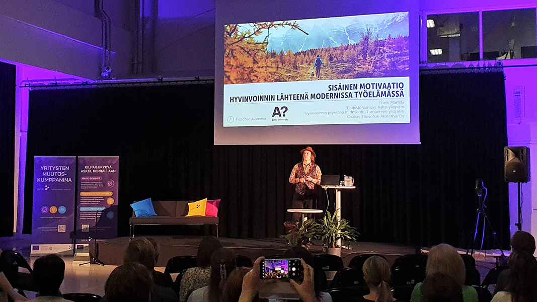 BIC Inspiration Frank Martela (c) Hanna Rissanen Web Frank Martela seisoo esiintymislavalla. Lavan takana esitys heijastettuna valkokankaalle.