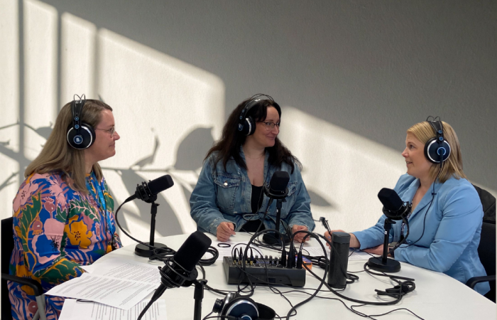 Petra Sippola, Mari Viljanen ja Minttu Porri istuvat pyöreän pöydän äärellä. Kaikilla on podcastiin tarvittavat kuulokkeet ja mikrofoni.