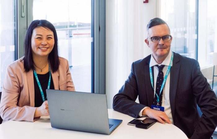 Woman and man sitting next to a desk and smiling for the picture.