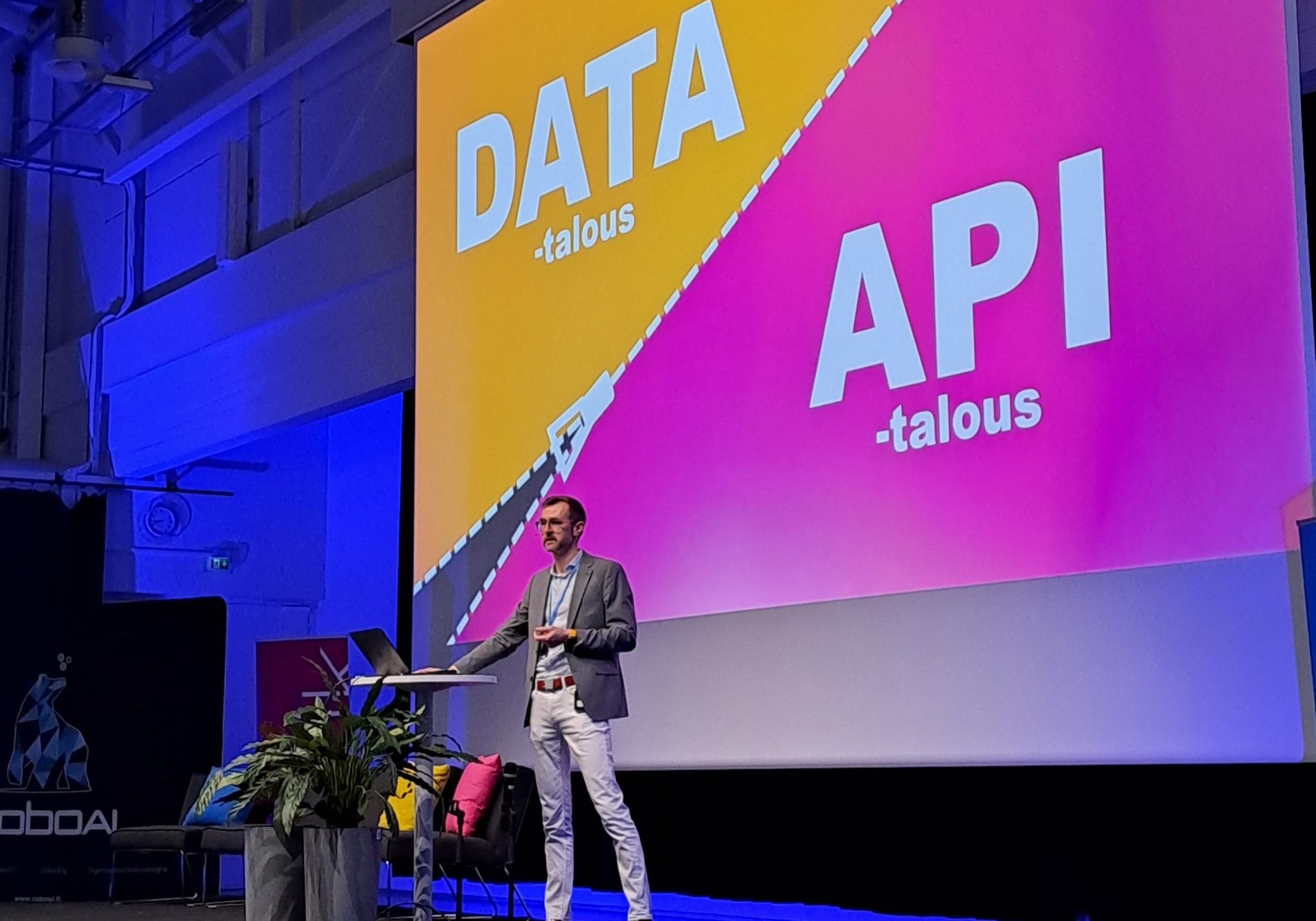 Tutkimuspäällikkö Mikko Pakkasela seisoo esiintymislavalla puhumassa. Taustalla PowerPoint -esityksessä aseteltuna sanat Data-talous ja API -talous.