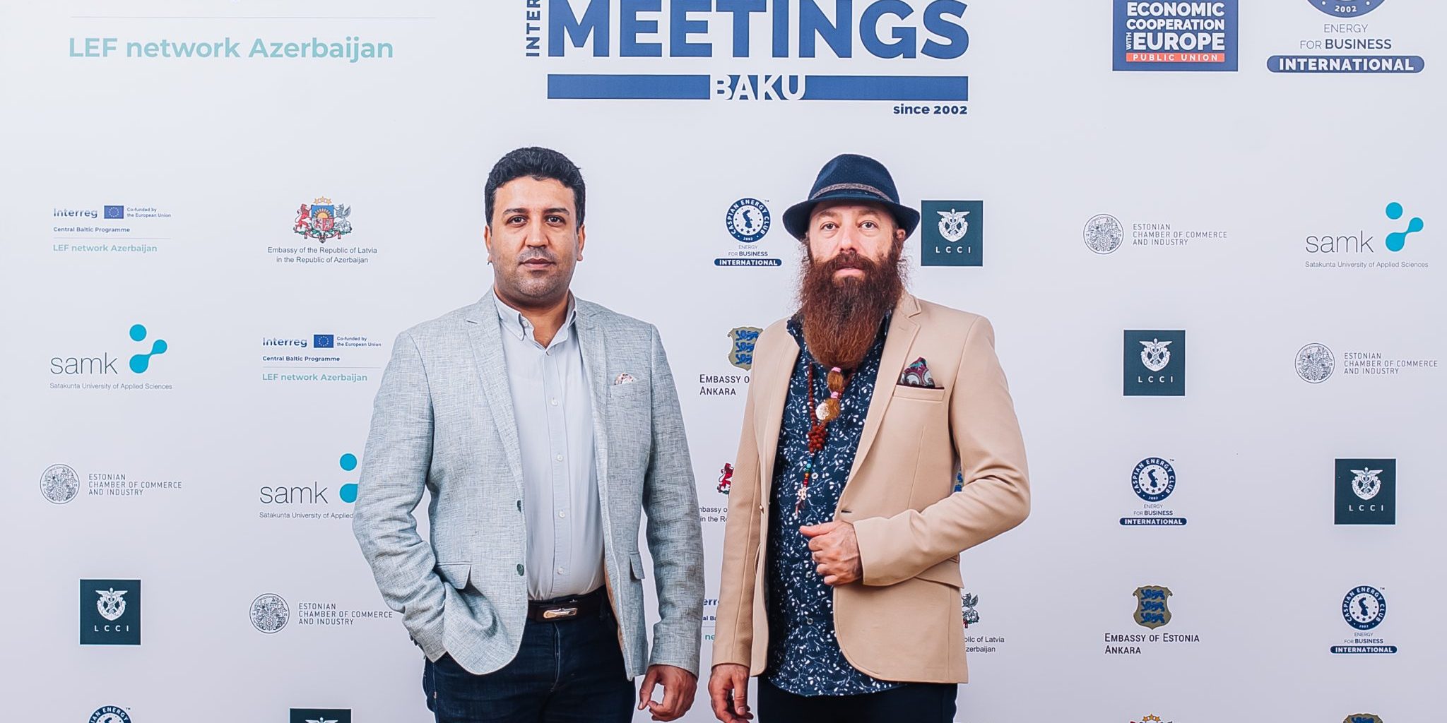 Two men standing in front of a meeting wall.