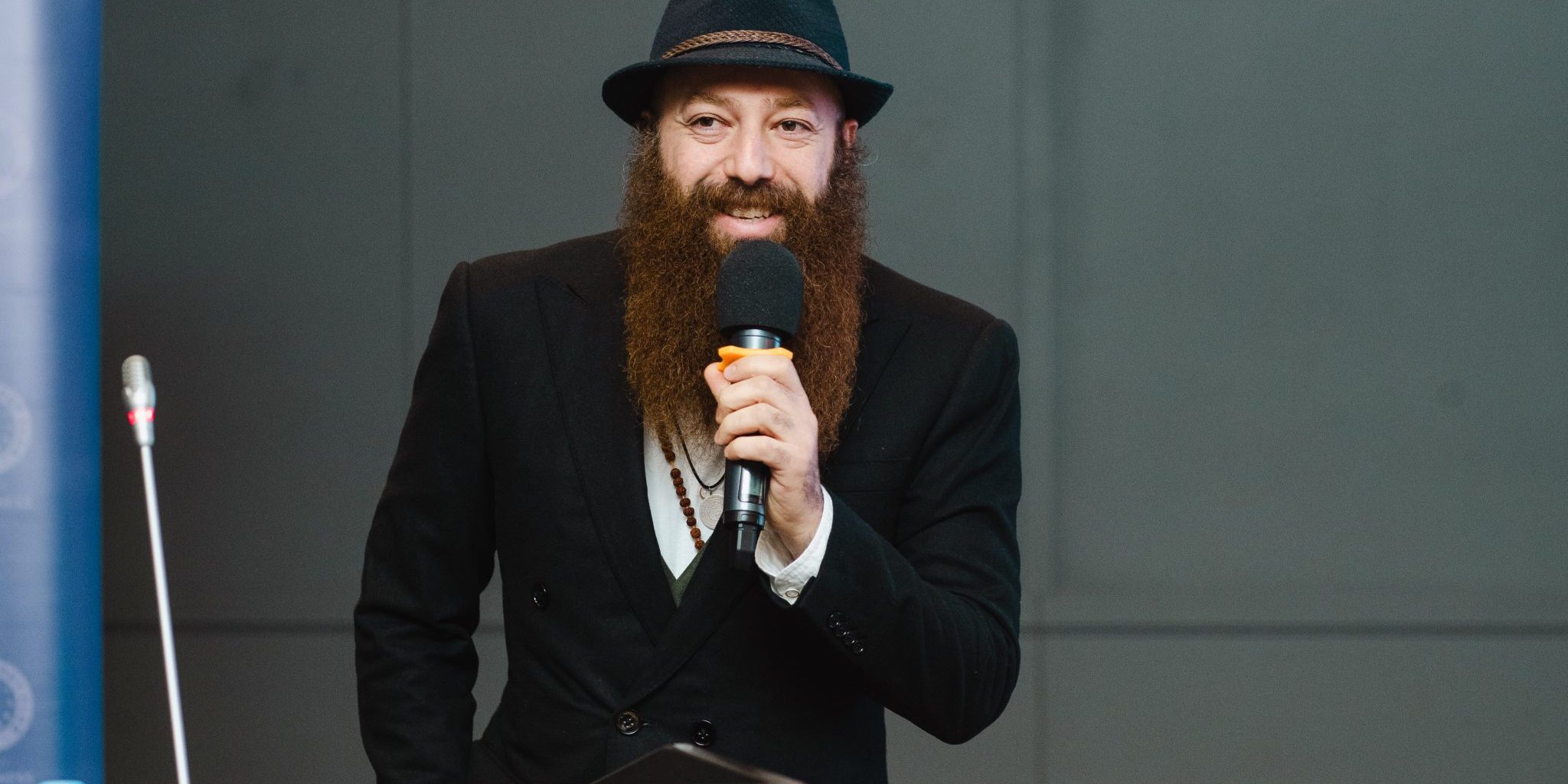 A bearded man talking to a microphone.