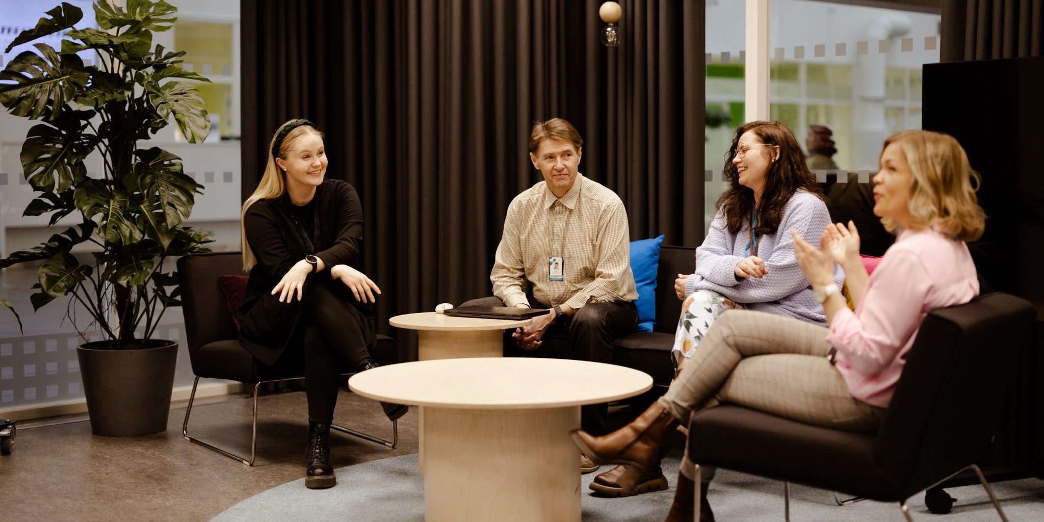 Four smiling people sitting on a sofa and armchairs.