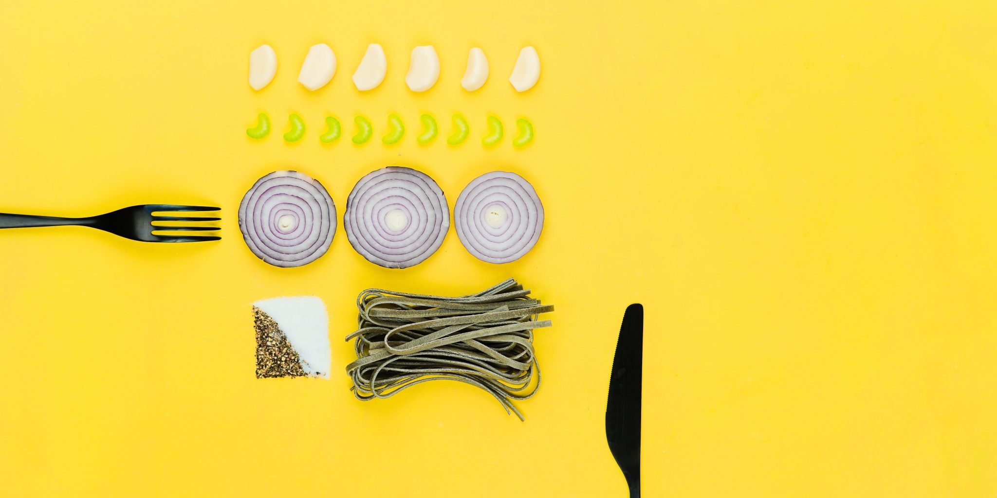 Fork and knife on a yellow background with some food items.